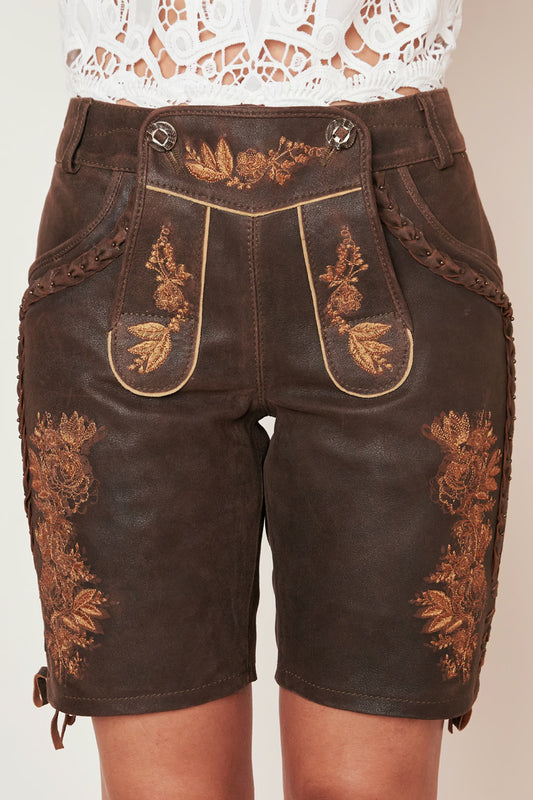 Dark brown leather shorts with ornate gold embroidery, decorative stitching, and braided details, shown on a model wearing a white lace top.